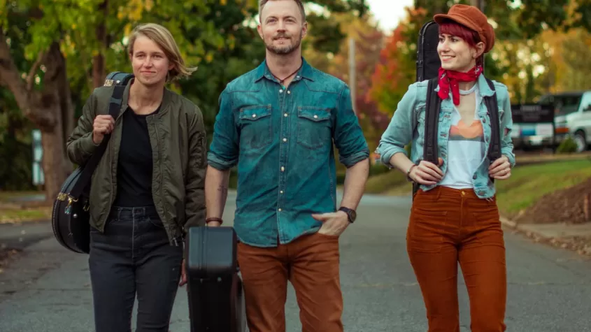 three people walking down a street carrying instrument cases